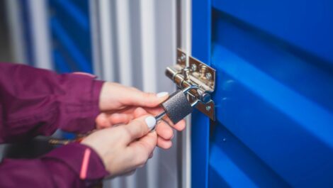 A person locking a blue self storage unit with a padlock