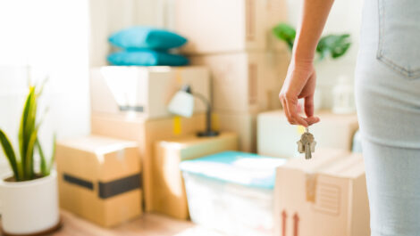 A woman standing in front of her moving boxes and plants in her new apartment, holding new keys.